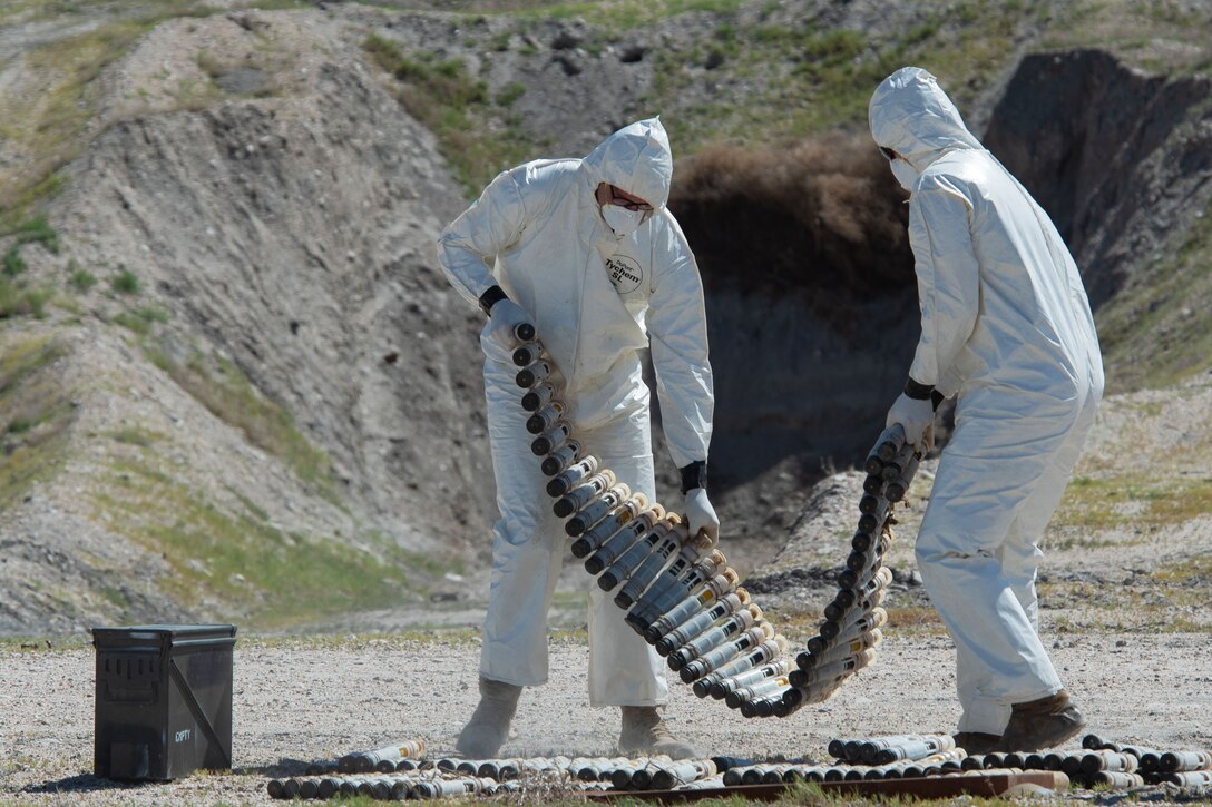 Two airmen in hazmat suits handle depleted uranium rounds.