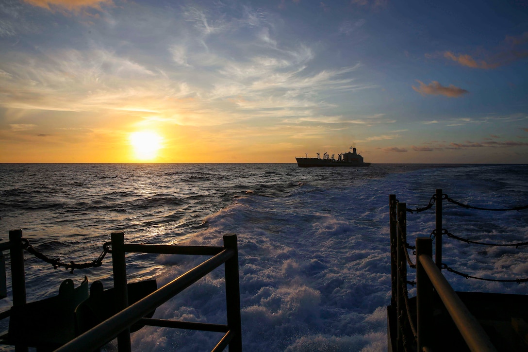 A ship travels through waters as the sun shines in the background.