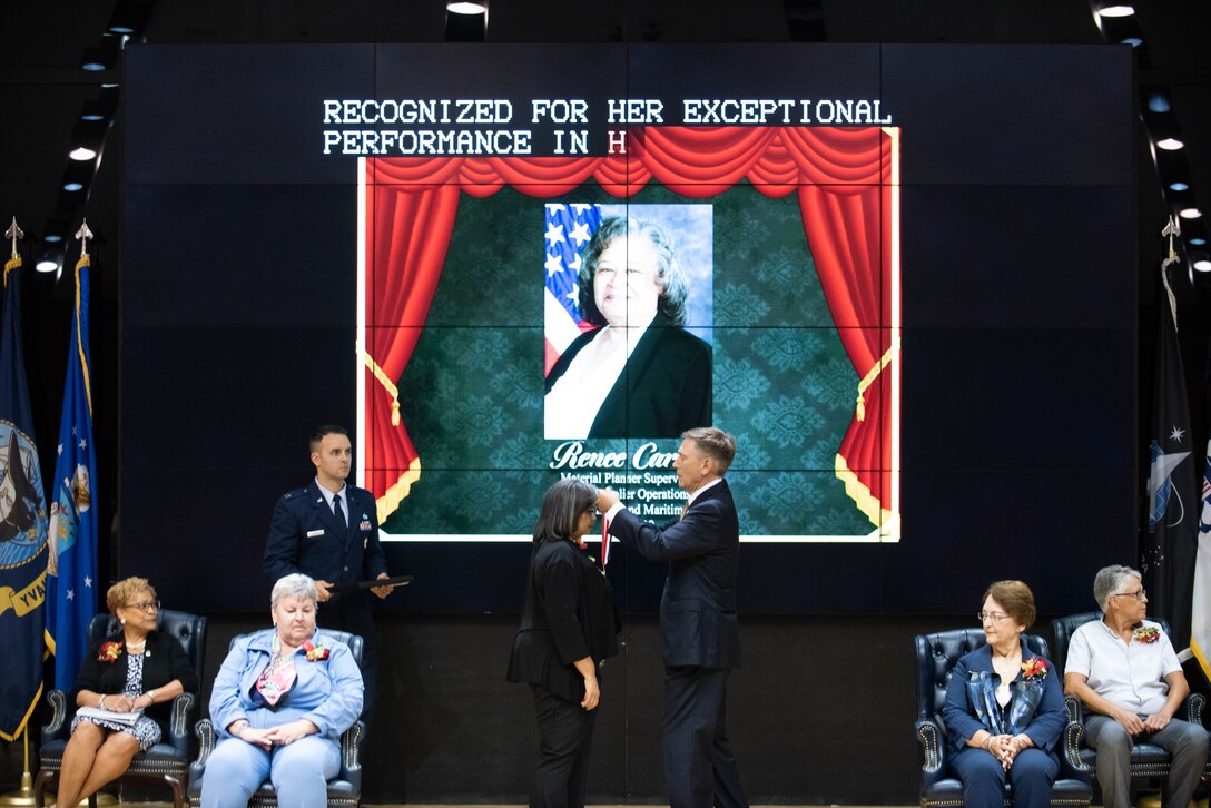 A man places a medal around the neck of a woman on stage.