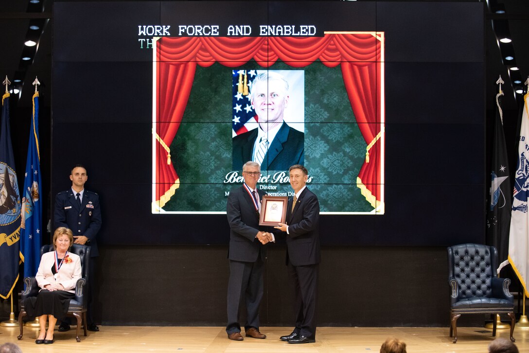 Two men hold a plaque on stage.