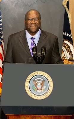 Black man in a suit stands in front of a podium with the presidential seal.
