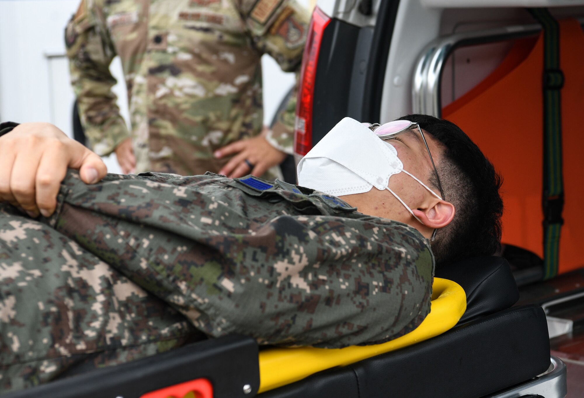 Republic of Korea Air Force Staff Sgt. Tong Ho Son, ROKAF Medical Group emergency medical driver, rest on a litter, at Kunsan Air Base, Republic of Korea, July 19, 2022. The 8th Medical Group held a bilateral immersion training with ROKAF to exchange litter carrying and response techniques to further improve their interoperability. (U.S. Air Force photo by Staff Sgt. Sadie Colbert)