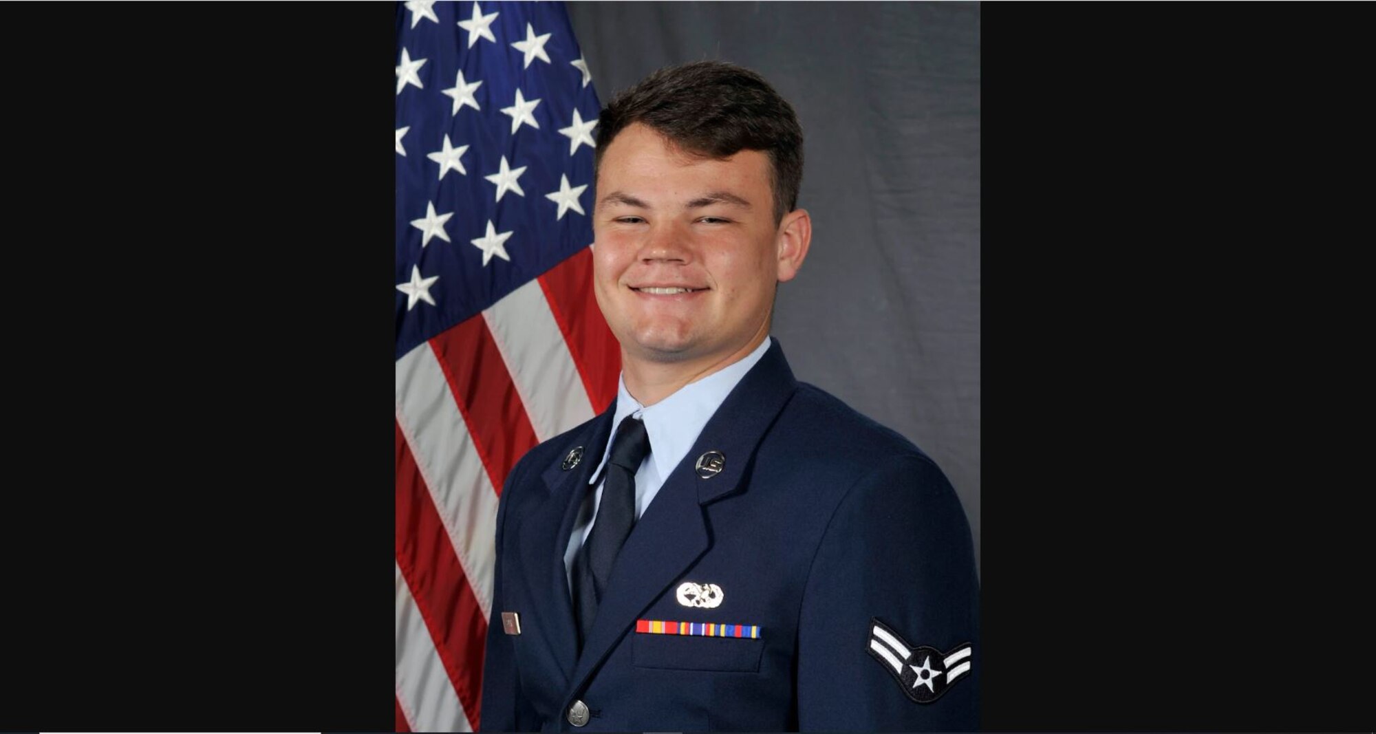 An Airman sits in front of a flag.