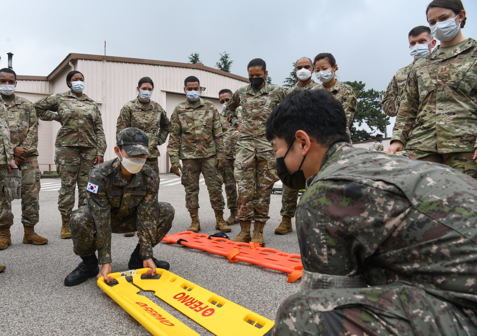 Republic of Korea Airman 1st Class Yeong Rang Kim, left, and Tech. Sgt. Mo Seh Yang, ROKAF Medical Group emergency medical technician, demonstrates using a litter carry, at Kunsan Air Base, Republic of Korea, July 19, 2022. Immersion trainings provide opportunities for U.S. and ROKAF members to work interoperability and enhance future mission fluidity. (U.S. Air Force photo by Staff Sgt. Sadie Colbert)