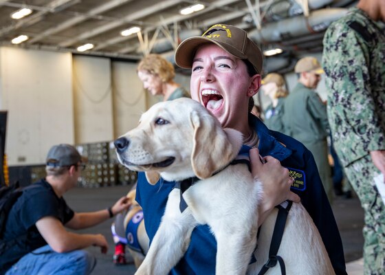 Ensign Sydney Hughes smiles while hugging a dog brought aboard USS George H.W. Bush (CVN 77).