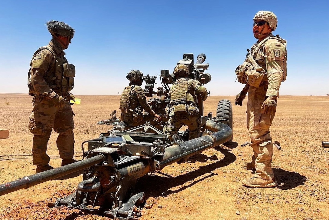 Four soldiers work with artillery on a barren landscape.