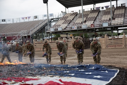 A line of soldiers throw folded American flags into a burn it during a flag retirement ceremony.
