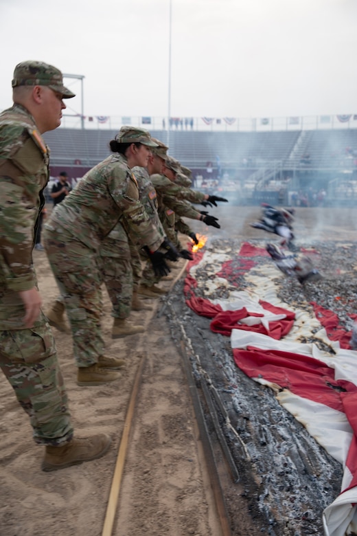 A line of soldiers throw folded American flags into a burn pit during a flag retirement ceremony.