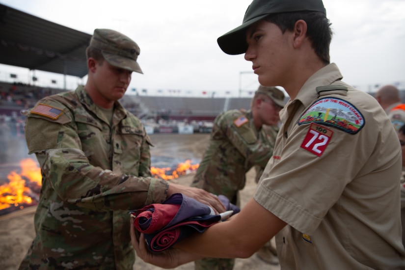 A boy scout hands a folded American flag to a soldier