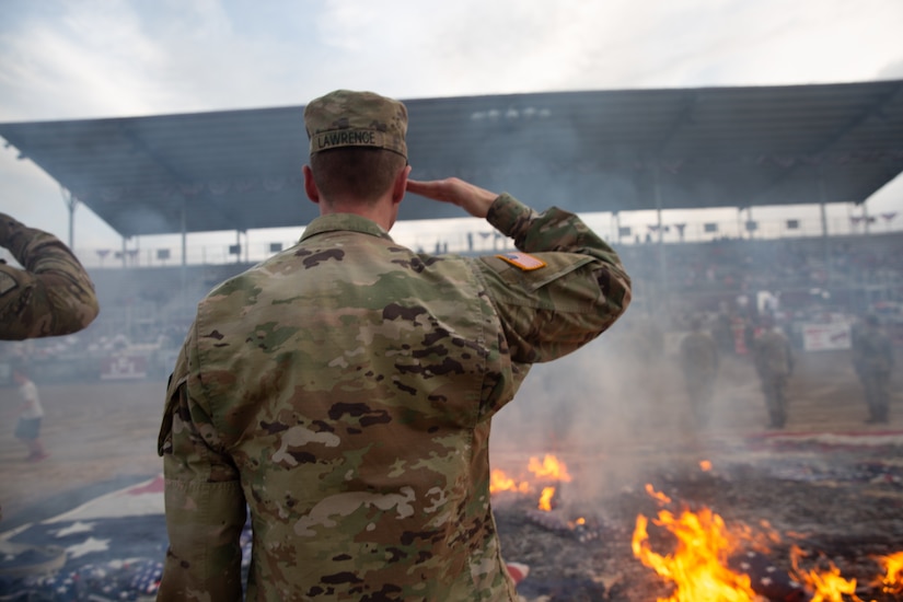 A soldier salutes burning American flags during a flag retirement ceremony.