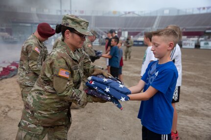 A young boy hands folded American flags to a female soldier.