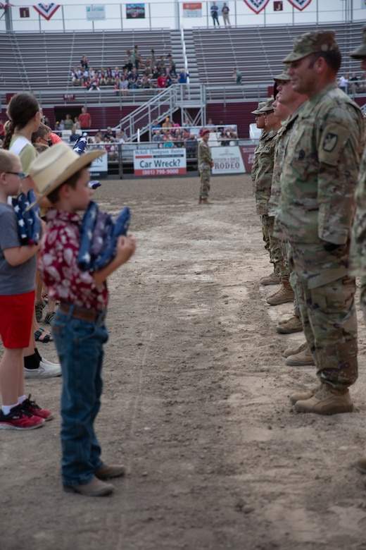 A young boy prepares to hand an American flag to a soldier.