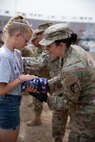 A young girl hands an American flag to a female soldier.