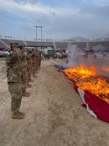 Soldiers salute burning flags in a fire pit during a flag retirement ceremony