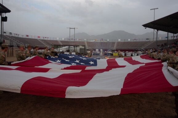 A group of soldiers carry a large flag to a burn pit during a flag retirement ceremony.