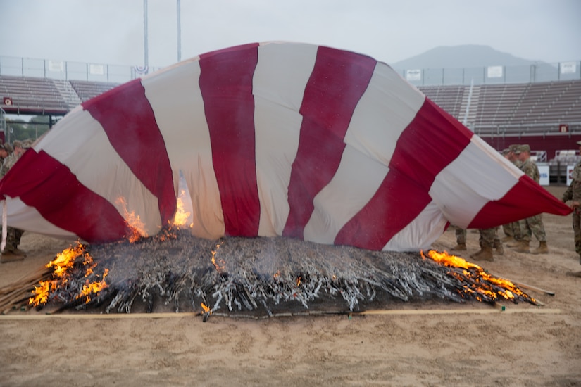An American flag is draped over a fire during a flag retirement ceremony