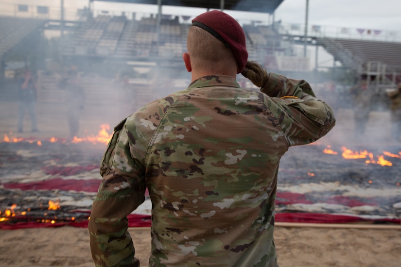 Soldier salutes flags in a fire pit during a flag retirement ceremony.