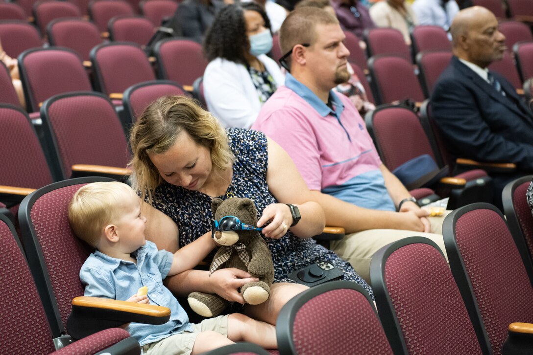 A woman entertains a baby in a large auditorium.