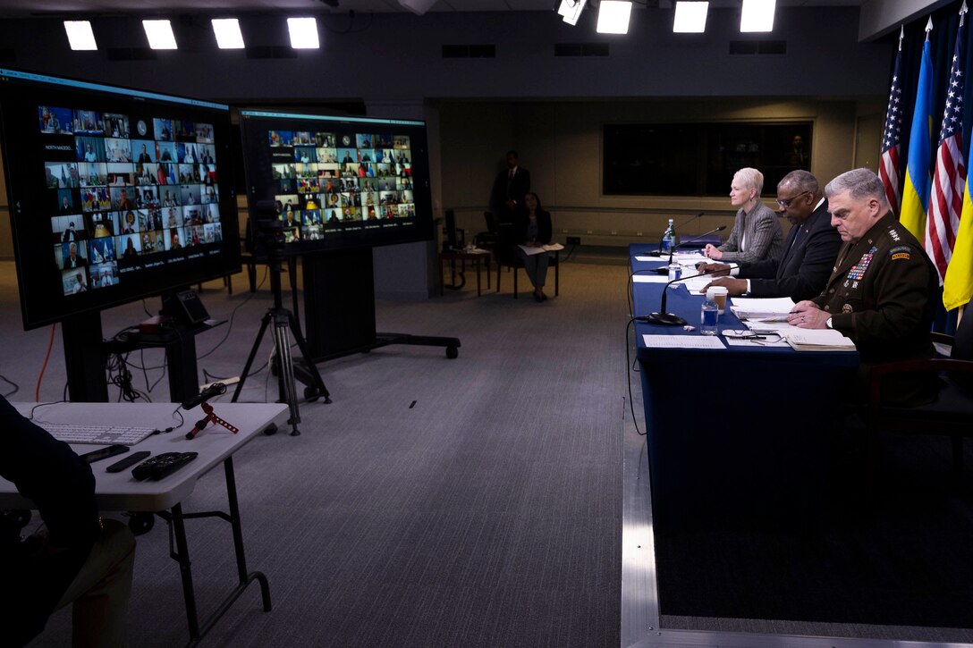 Defense secretary, Joint Chiefs chairman and civilian official sit at table facing two large screens.