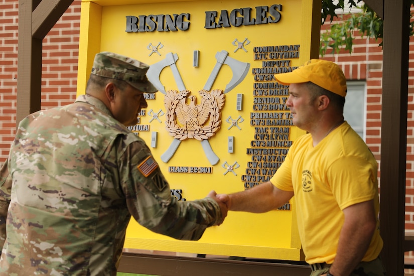 Warrant Officer Candidate Creighton Knopsnider shakes hands with Lt. Col. Tommy Guthrie, the commandant of the 166th Regiment Regional Training Institute, following the unveiling of the class sign at a sign, song, and hat ceremony at Fort Indiantown Gap, July 17, 2022. (U.S. Army National Guard photo by Capt. Leanne Demboski)