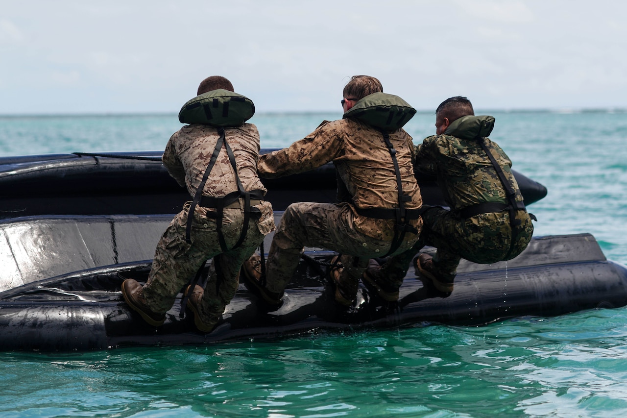 Three service members work to flip an inflatable boat on water.
