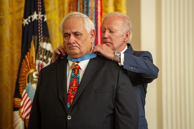A man puts a medal around another man’s neck.