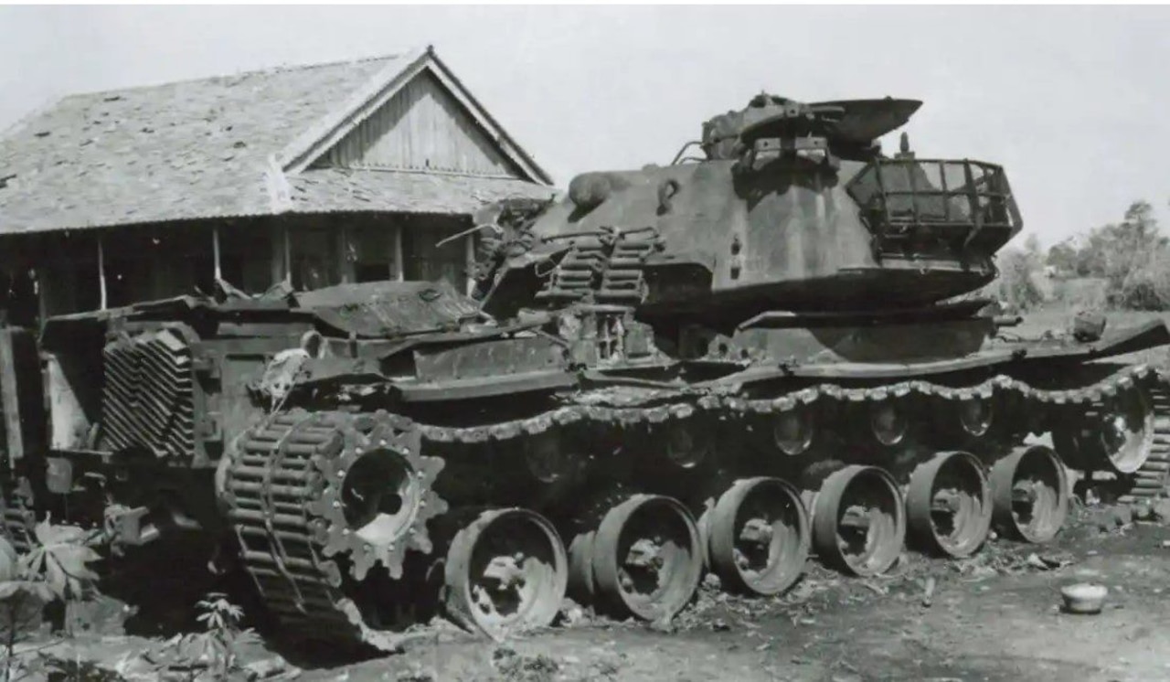 A damaged tank sits near a small house.