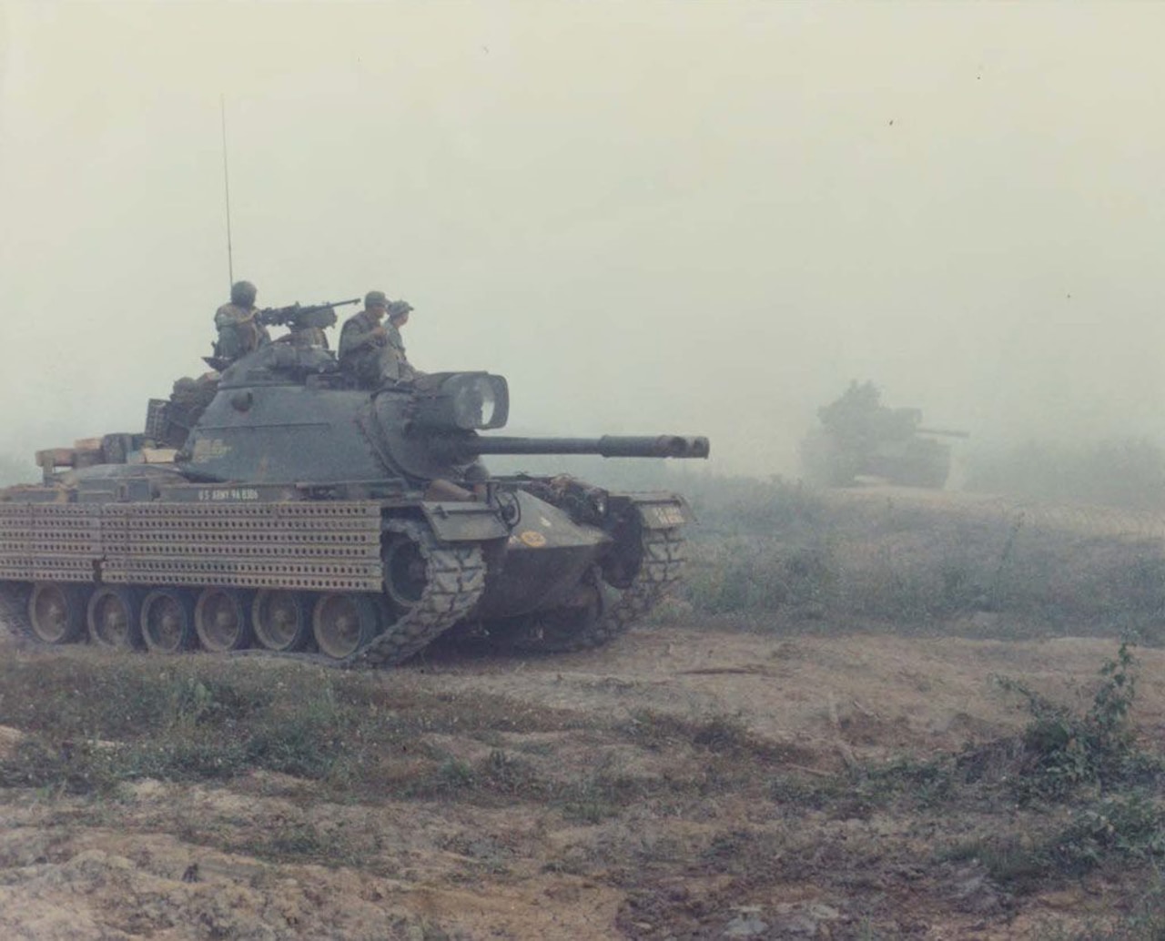 Three soldiers sit on top of a tank and look into the distance.