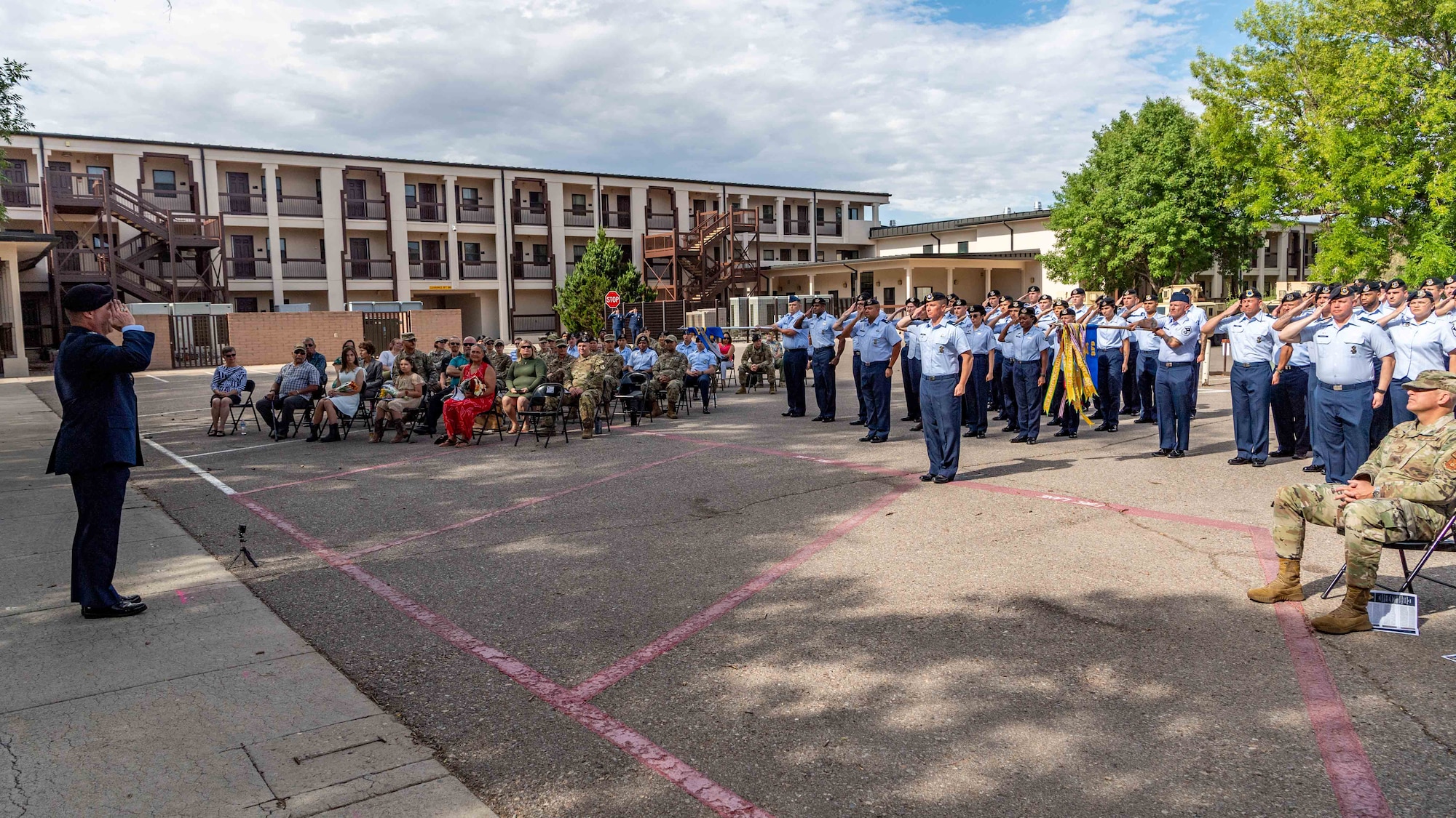 A group of Airmen and visitors listen to a speech outside.