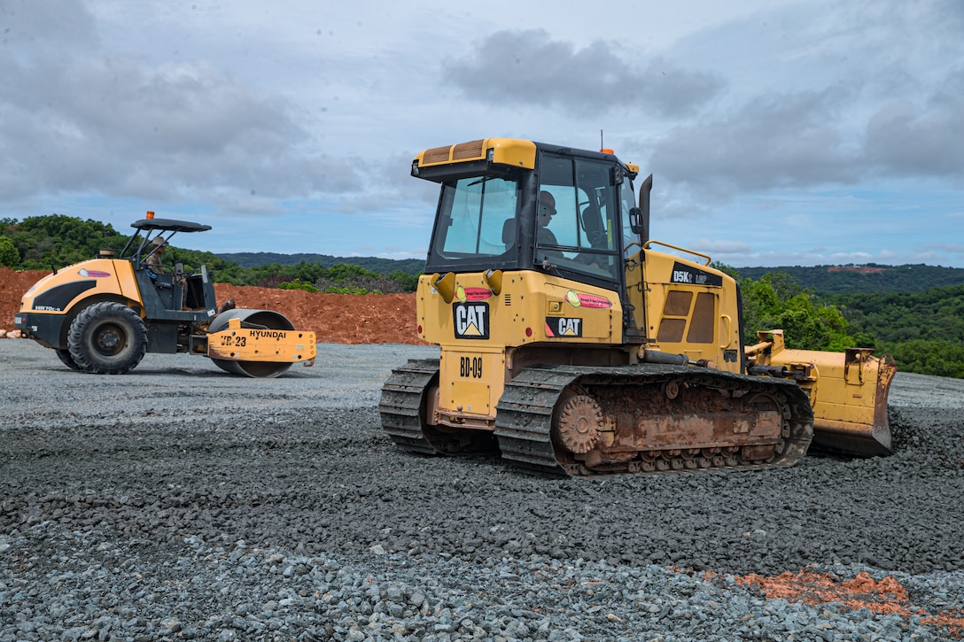 U.S. Marine Corps Lance Cpl. Shane Cooke, left, an engineer equipment operator, and Pfc. Brayan Cordovagonzalez, a heavy equipment operator, both with Task Force Koa Moana 22, I Marine Expeditionary Force, flatten gravel during construction of the Joint Range Complex in Ngchesar, Republic of Palau, July 5, 2022. The Joint Range Complex will provide the U.S. military and Palauan law enforcement agencies a place to sharpen their skills and improve marksmanship capabilities, strengthening readiness and interoperability in support of U.S. Indo-Pacific Command’s strategic and operational objectives.