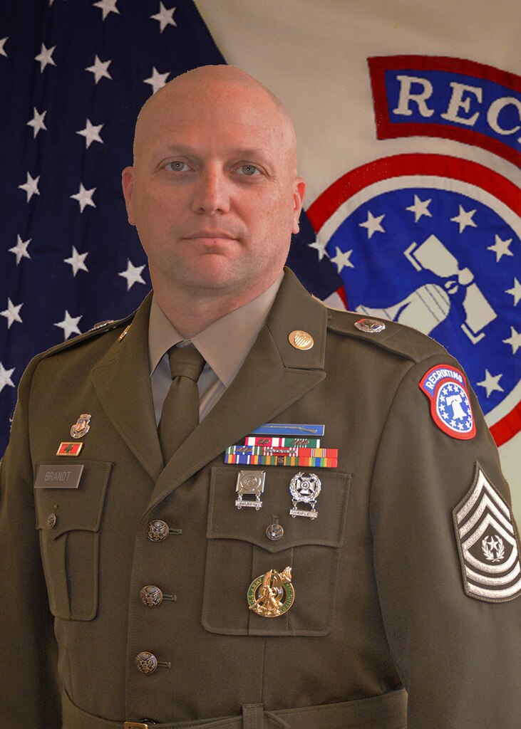 Soldier standing in front of flag backdrop.