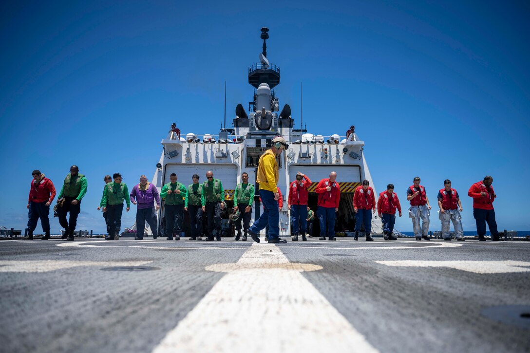 A row of sailors and coast guardsmen do a walking check on the deck of a ship.