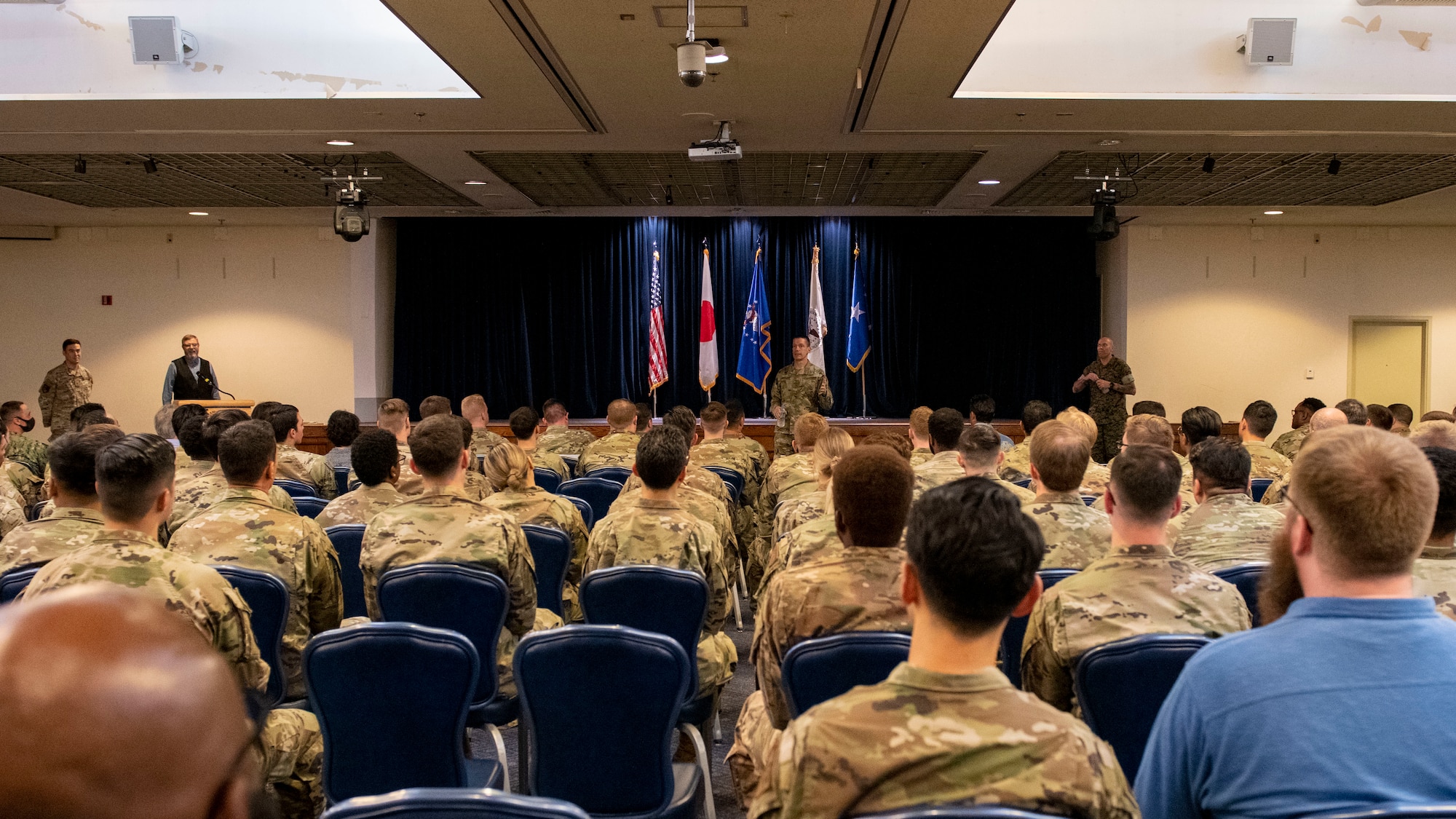 many uniformed people sitting, while facing a stage