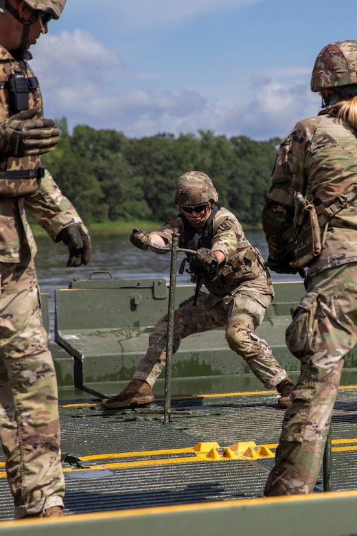 A soldier strains while manipulating a pole-type device on a bridge.