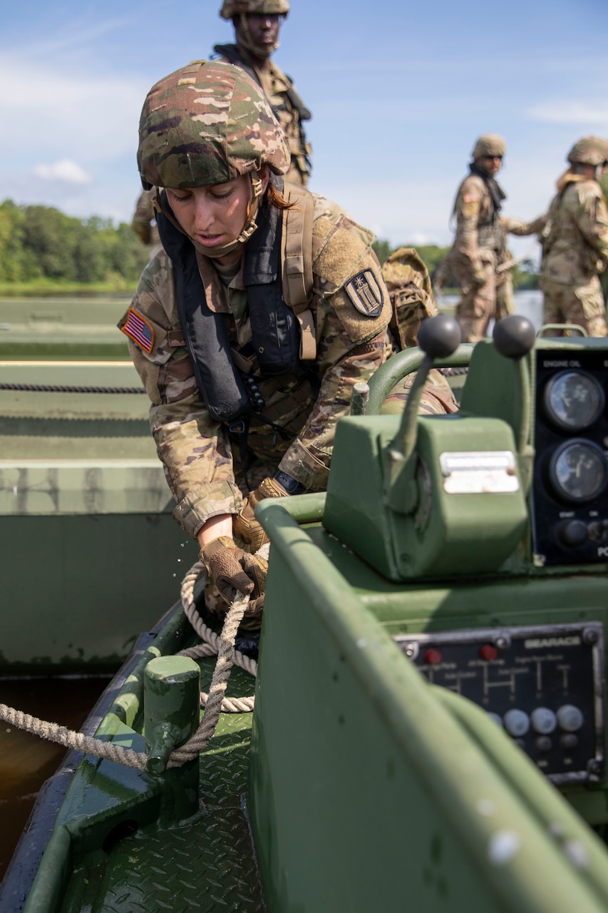 A soldier manipulates a rope on a boat.