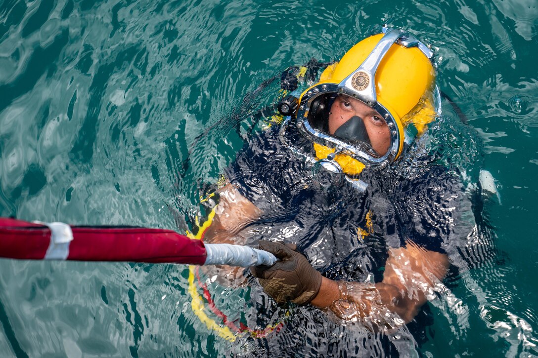 A sailor in the water wearing scuba gear looks upwards.