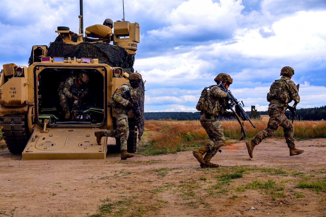 Armed soldiers exit a military vehicle on a dirt path in a field.