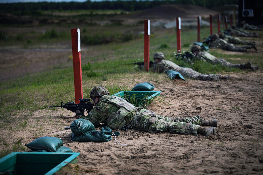 A line of soldiers holding M4 rifles lay prone and aim their weapons.