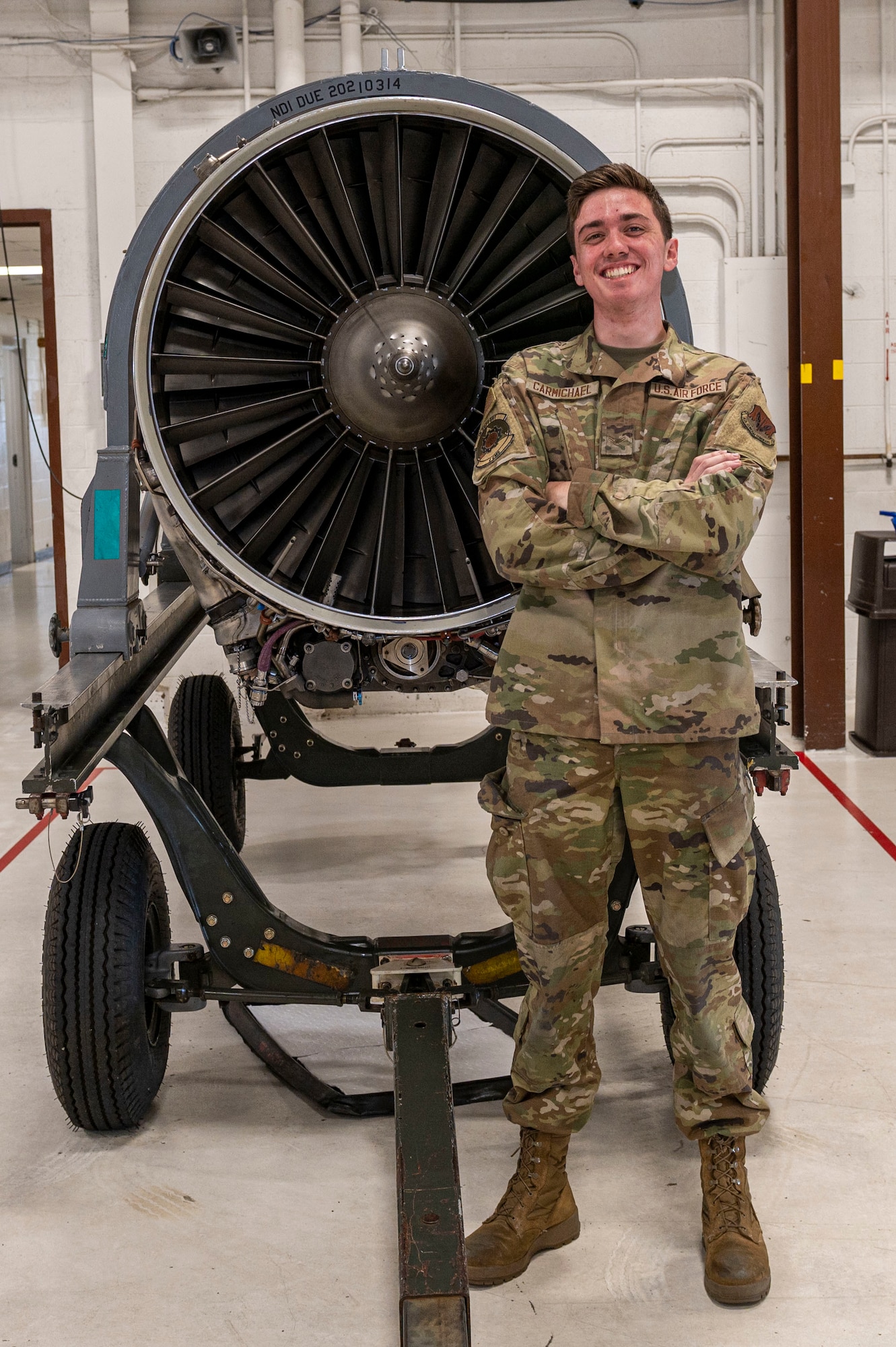 Airman 1st Class Alasdair Carmichael, 4th Component Maintenance Squadron aerospace propulsion journeyman, poses with an F-15E Strike Eagle engine at Seymour Johnson Air Force Base, North Carolina, July, 13, 2022. Carmichael is from Denny, Scotland and joined the U.S. Air Force to pursue his career goal and become an astronaut. (U.S. Air Force photo by Airman 1st Class Sabrina Fuller)