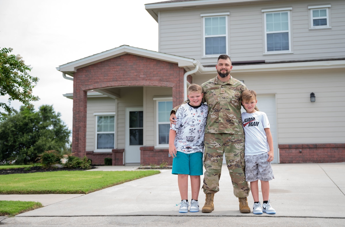 An Airman in uniform stands in front of a home with two young boys.