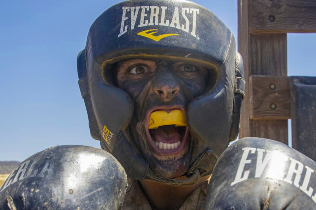A Marine wearing a helmet and boxing gloves yells.