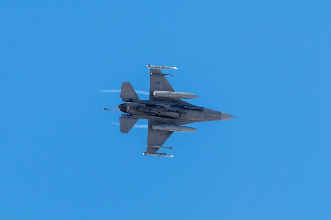 A military jet flies against a deep blue sky.