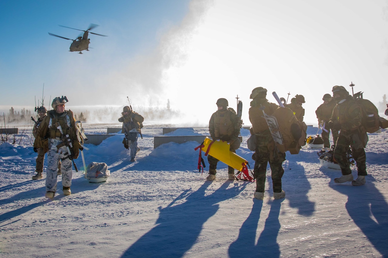 Service members stand in the snow while helicopters fly above.