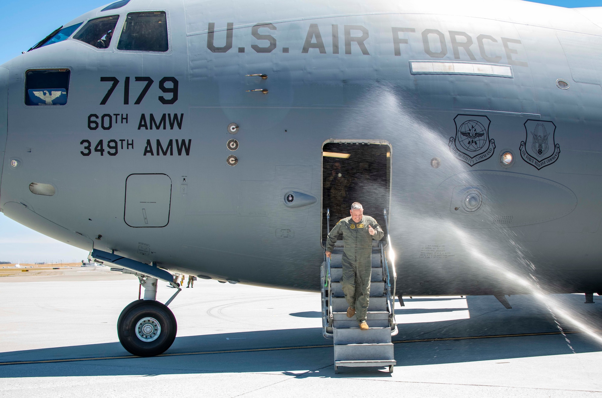 The 60th AMW commander walks down the stairs of an airplane.