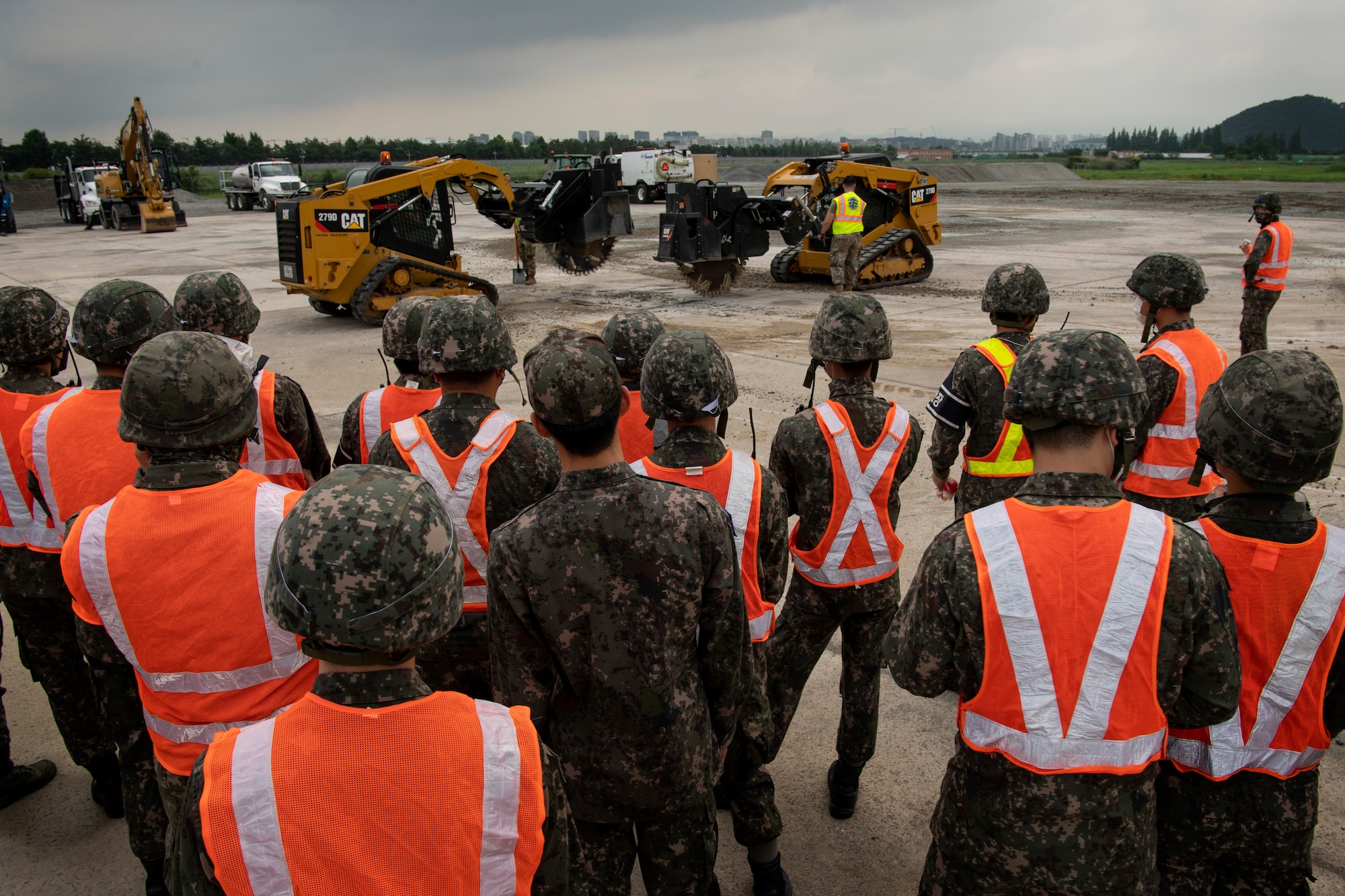 Members of the Republic of Korea Air Force (ROKAF) watch as United States Air Force (USAF) Civil Engineers use Compact Track Loaders with saw attachments to cut cement around craters during rapid airfield damage repair training, July 19, 2022 at Gwangju Air Base, Republic of Korea.