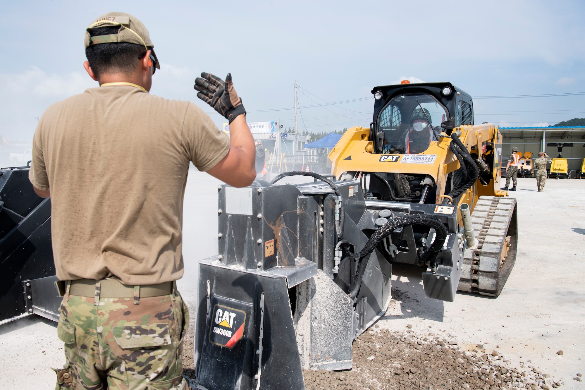 U.S. Air Force Senior Airman Sebastian Nunez, an Operations Management Journeyman, directs a member of the Republic of Korea Air Force operating a Compact Track Loader with saw attachment during rapid airfield damage repair training, July 19, 2022 at Gwangju Air Base, Republic of Korea.