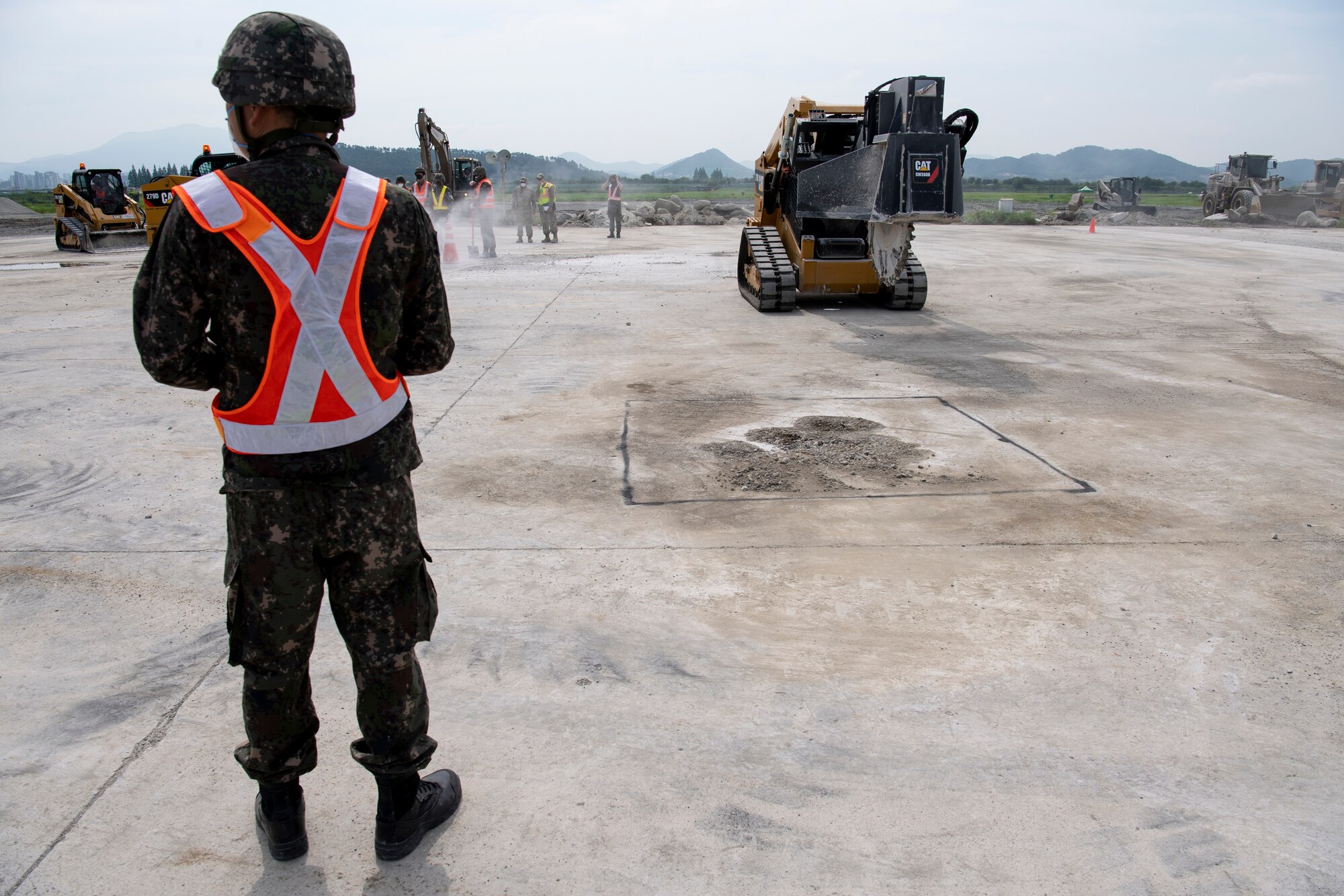 Civil Engineers from the Republic of Korea Air Force (ROKAF) and United States Air Force (USAF) use Compact Track Loaders with saw attachments to cut cement around craters during rapid airfield damage repair training, July 19, 2022 at Gwangju Air Base, Republic of Korea.