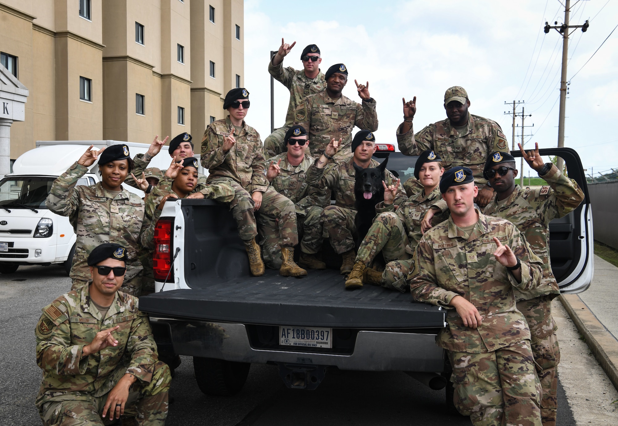 Military members pose with a military working dog in the back of a pick-up truck.