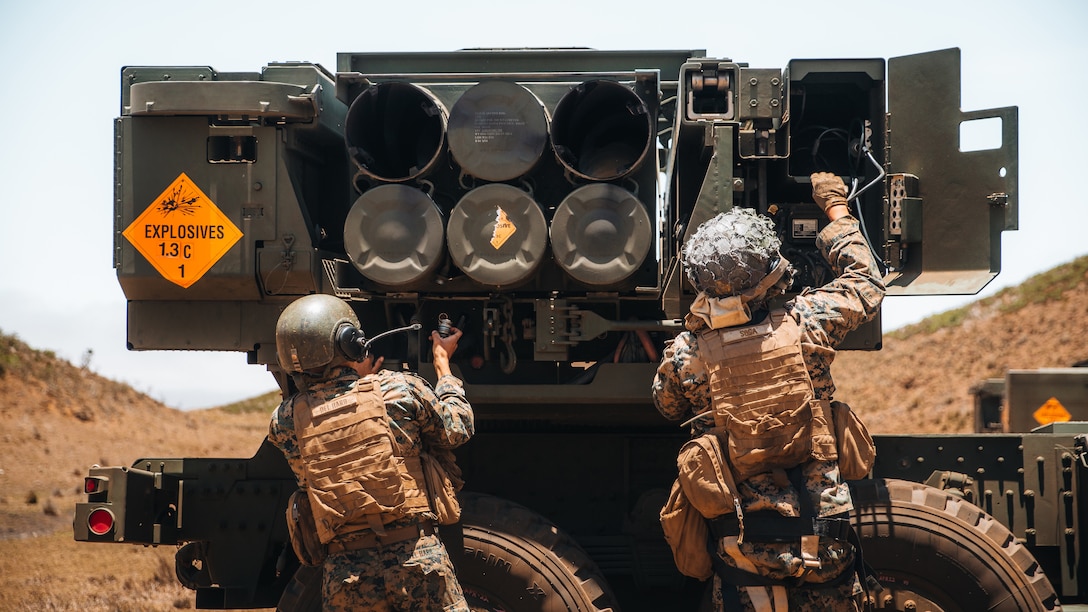 Two service members operate a large weapons system.