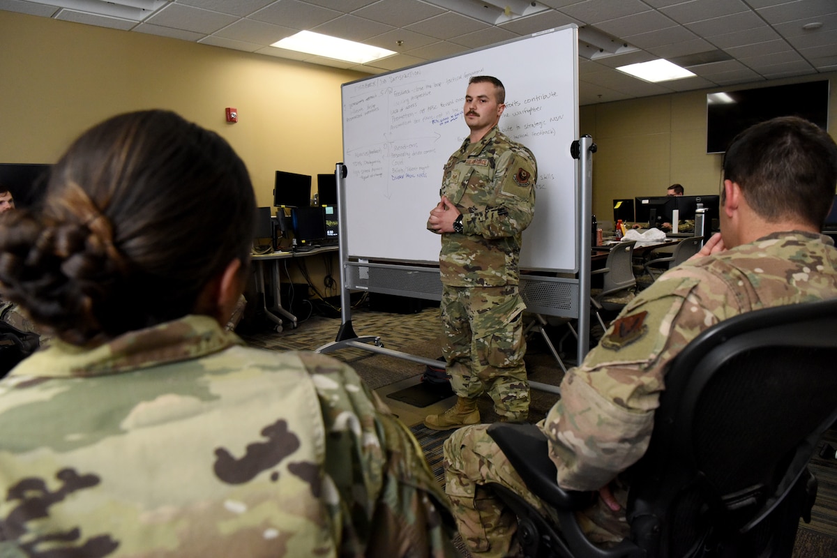 An Airman briefs his fellow teammates in front of a white board.